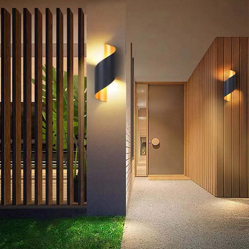 Black and gold curved wall lights beside timber slats, plants and an entry passage