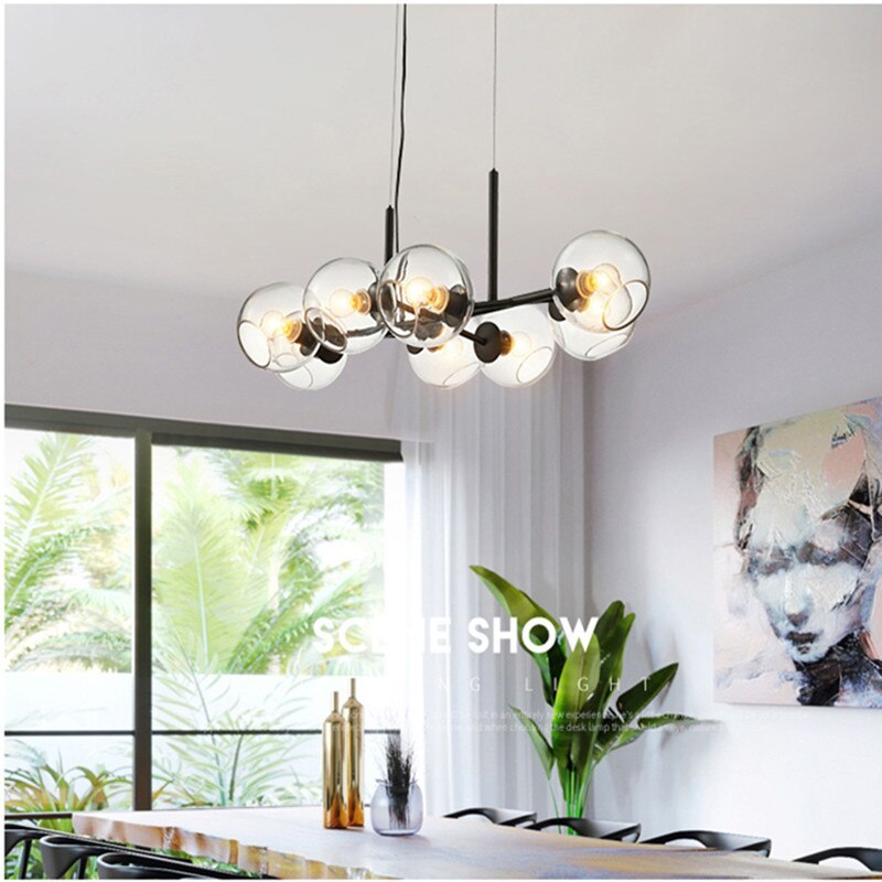 Black Valentina clear-globe pendant above a dining table beside a plant, window and wall artwork