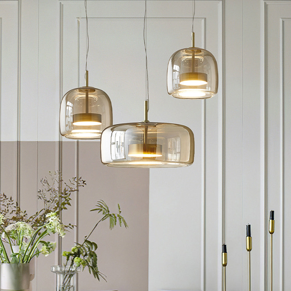Three Hailie glass pendants with gold-tone inner discs, two compact shades above a wide shade, beside candlesticks