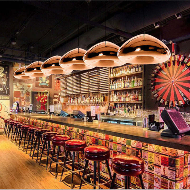 Rose-gold reflective dome pendants above a bar with red stools