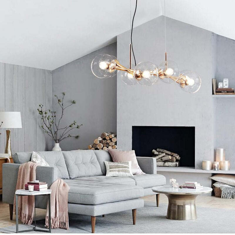 Gold clear-globe pendant over grey sofa, round coffee table and fireplace with stacked logs beneath an angled ceiling