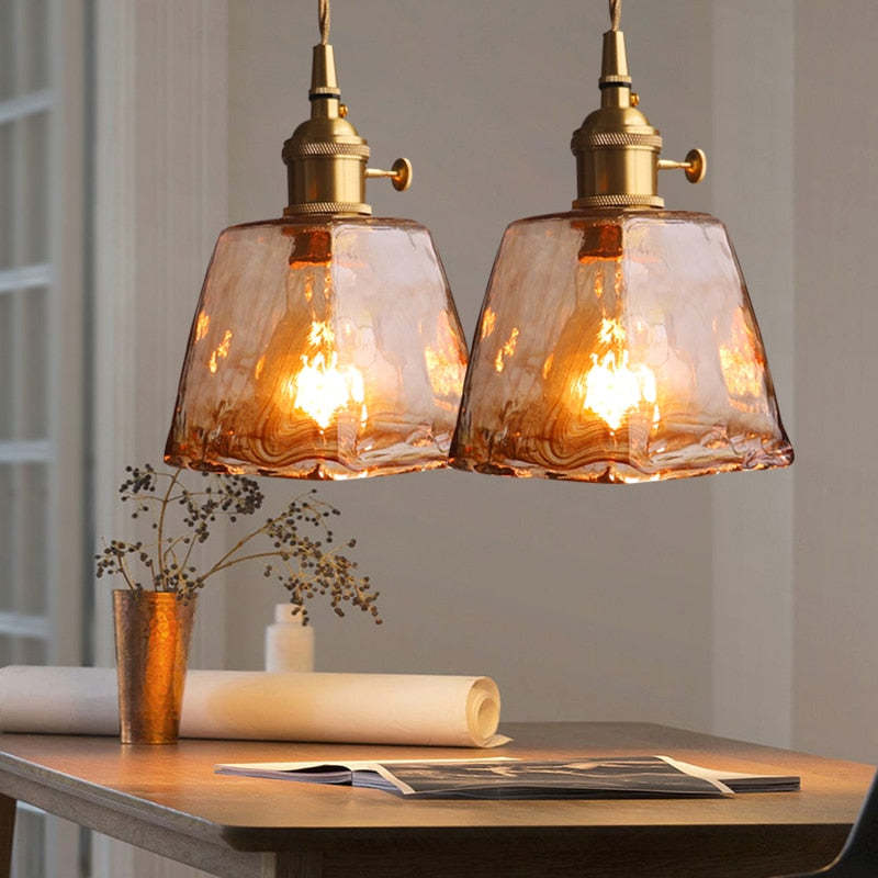 Two textured amber glass pendants above a table with a vase and an open magazine
