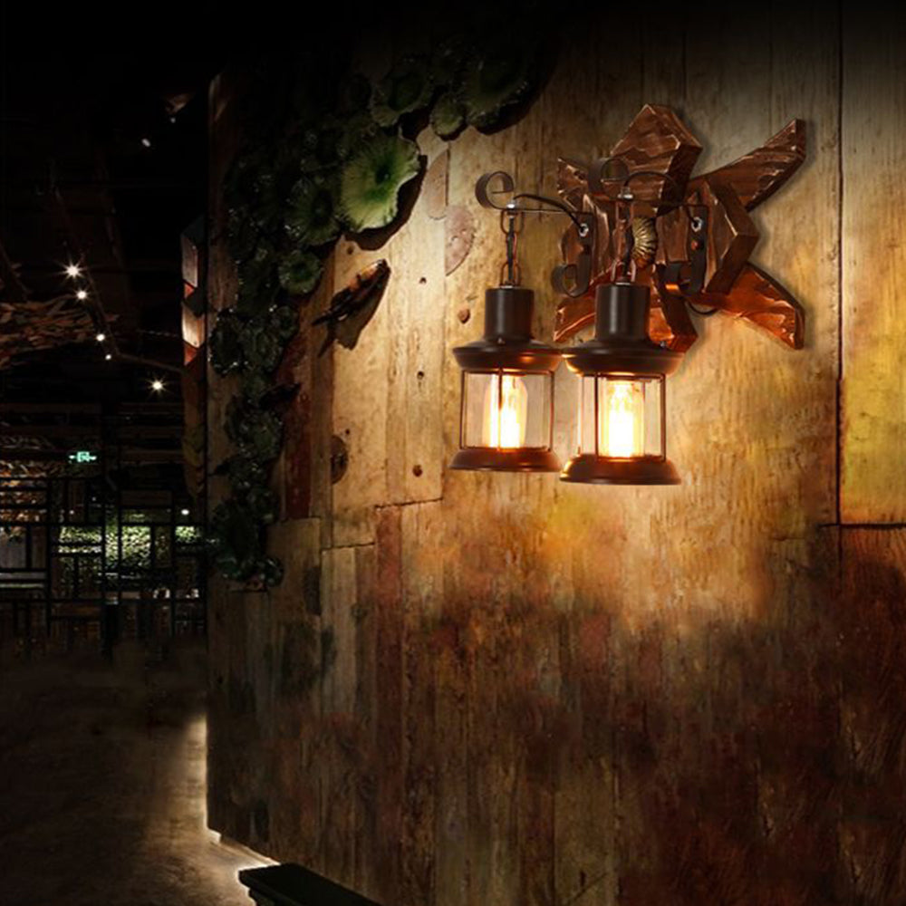 Austin double lantern wall light illuminated against a rustic wall beside plants.