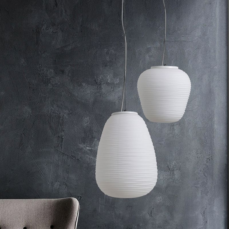 Tall and compact white ribbed pendants before a grey textured wall and upholstered chair