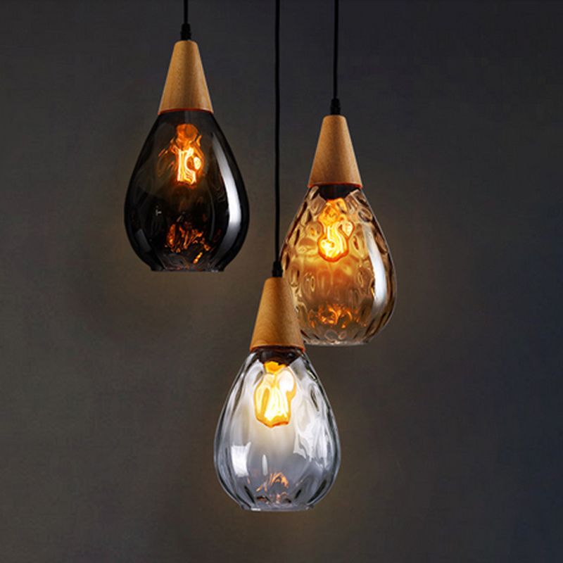 Three narrow Avi pendants in smoke gray, amber and clear glass with wood tops against dark background