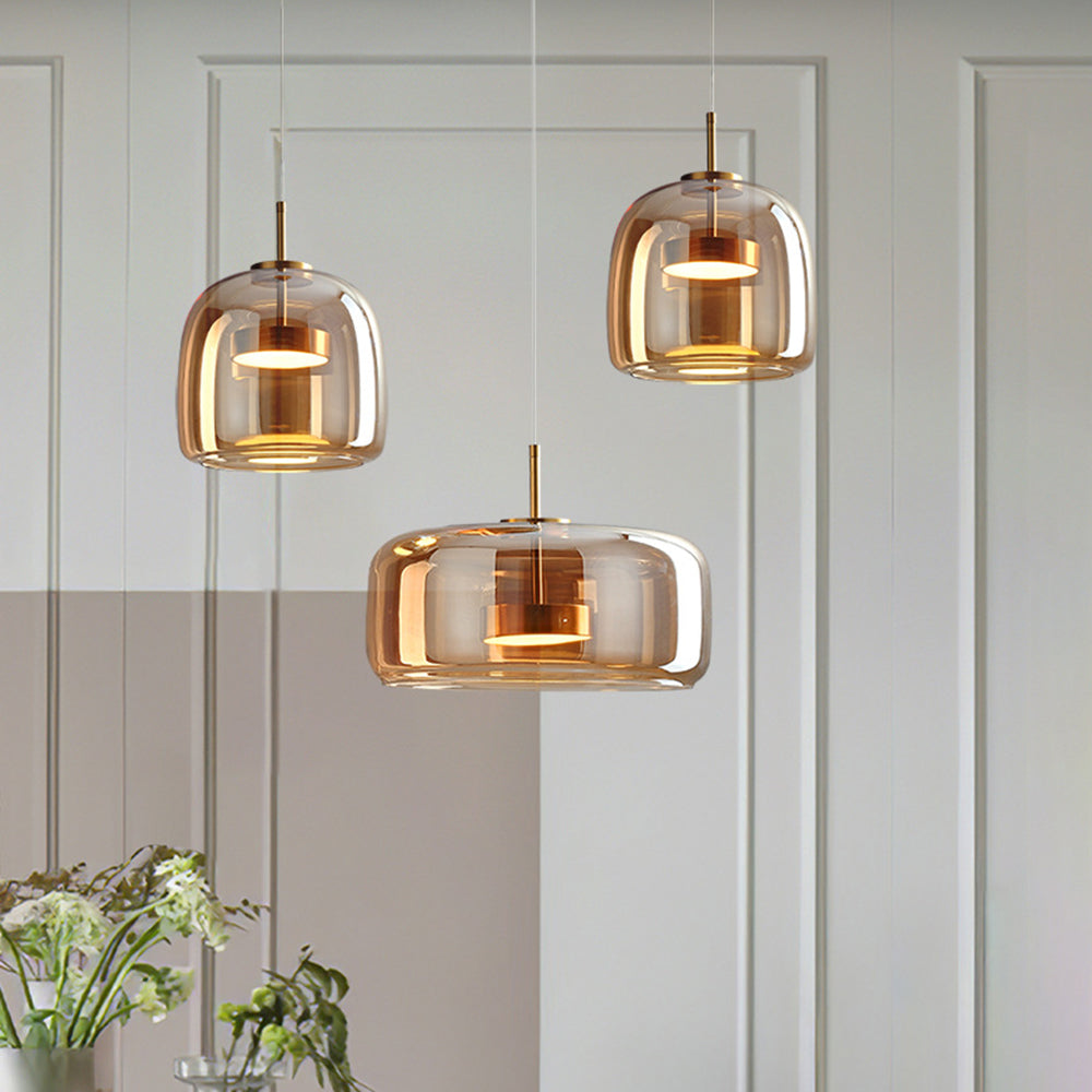 Three amber Hailie pendants: two taller compact shades above a wide low shade, beside flowers against paneled wall