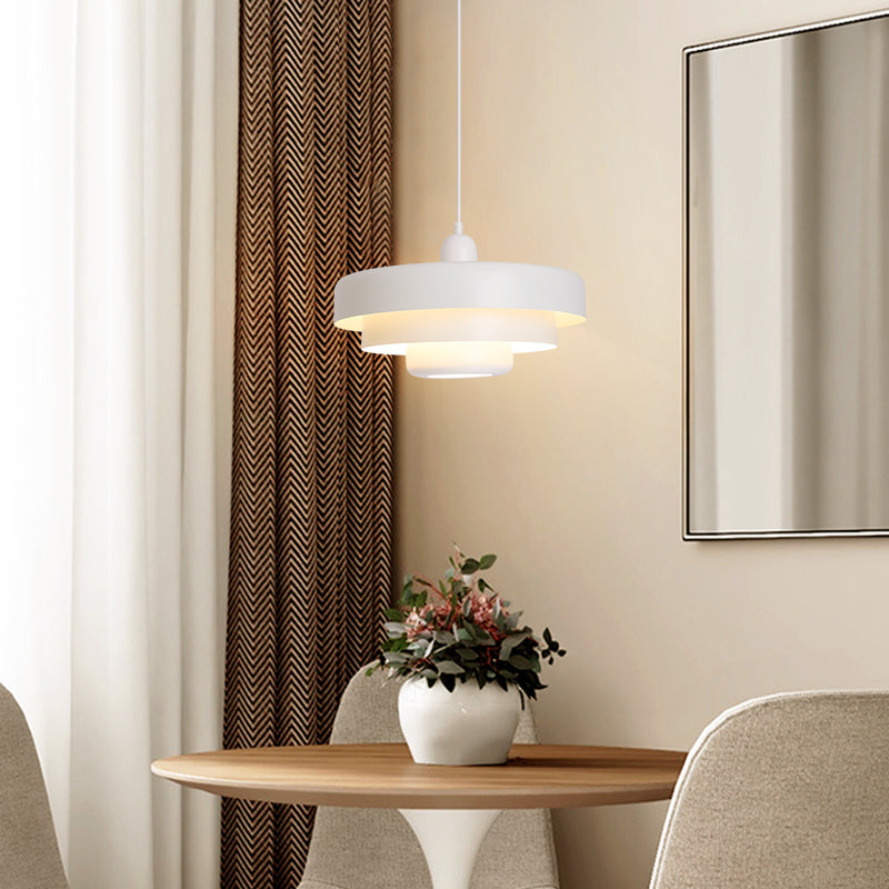 White tiered pendant light above a round wooden table with flowers, chairs and patterned curtains