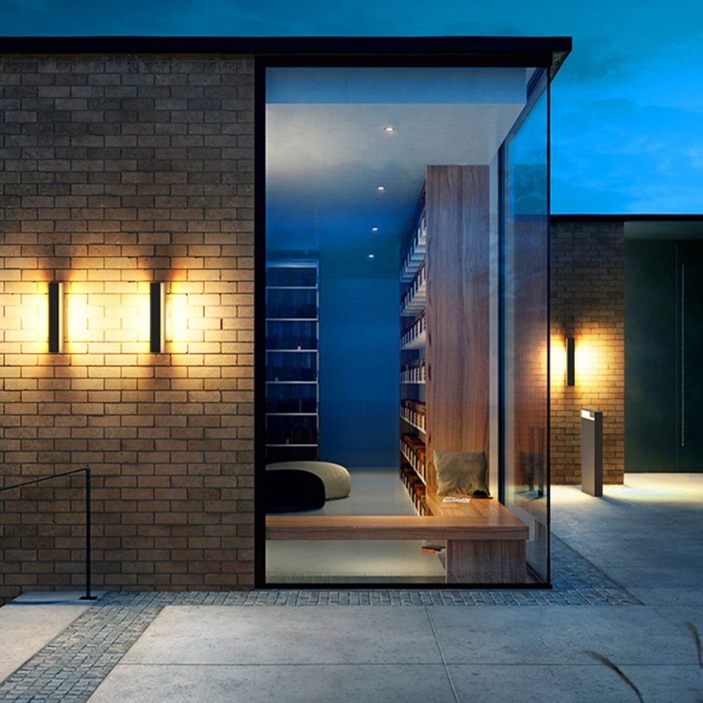 Black upright wall lights casting warm-looking light on a brick exterior beside a glass corner