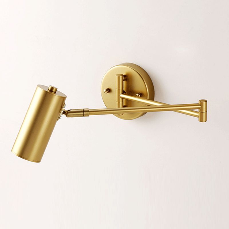 Brady Gold cylindrical wall light with crossing rods, outer pivot and round plate against a pale wall