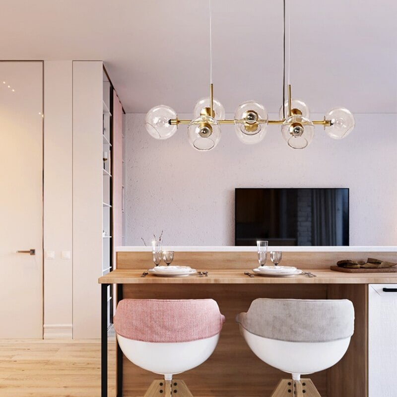 Gold clear-globe pendant above timber breakfast counter, set plates and two white chairs with pink and grey backs