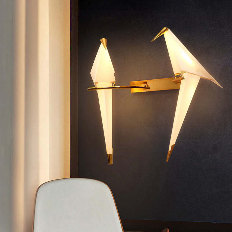 Angled two-bird Clifford wall light near a curtain and chair, with birds in different poses on a gold-tone perch