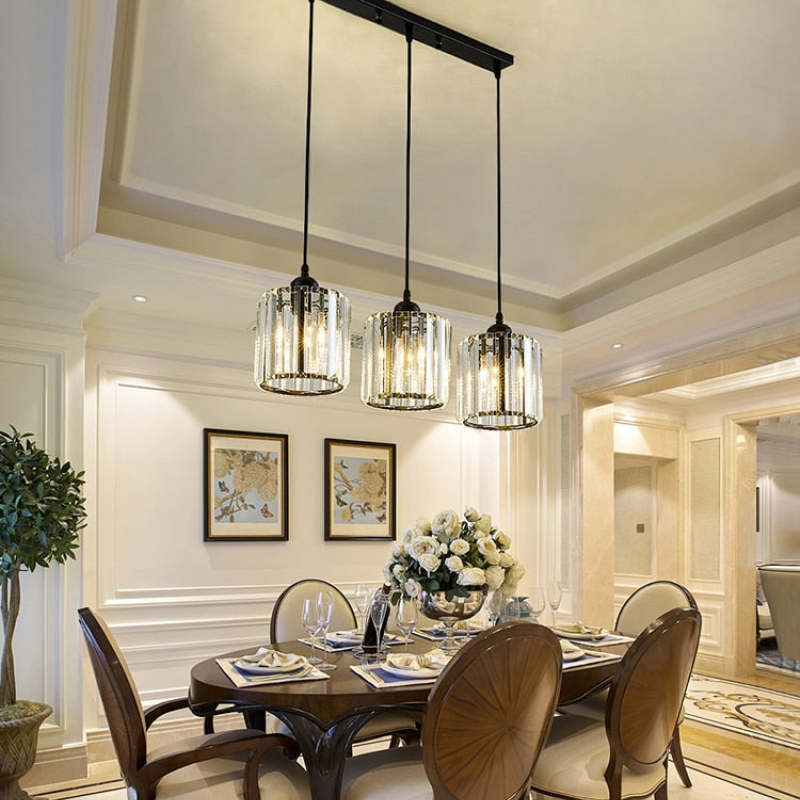 Three black Herbert cylindrical glass pendants in a line above a dining table with wooden chairs and flowers