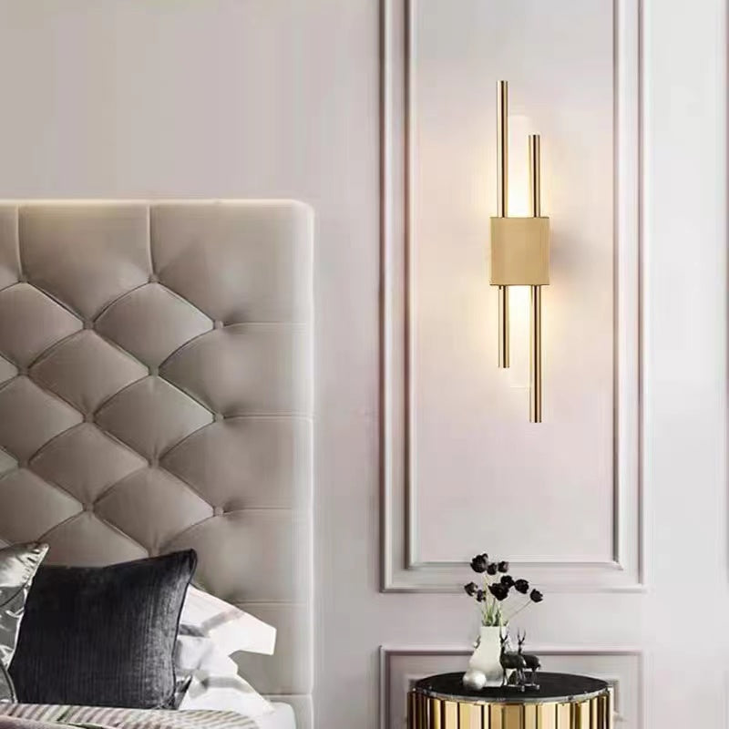 Gold Alana wall light on a pale paneled wall beside an upholstered headboard and rounded bedside table