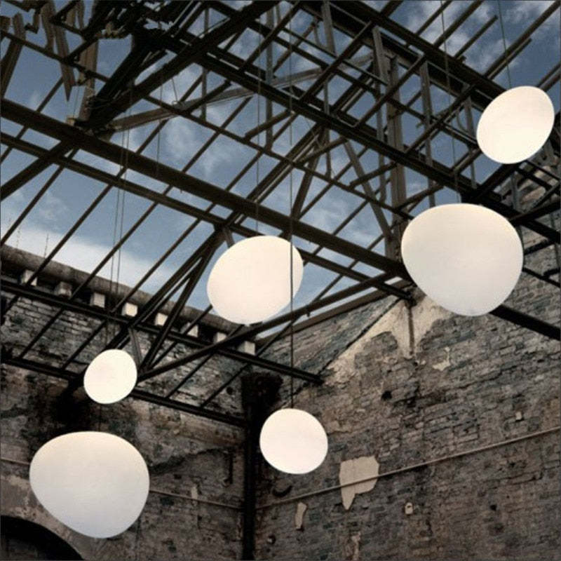 White pebble-shaped pendants at staggered heights beneath dark roof trusses and glass above rough masonry walls