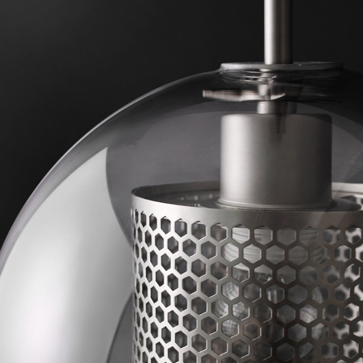 Close view of a silver-coloured perforated cylinder and holder inside a curved clear glass shade