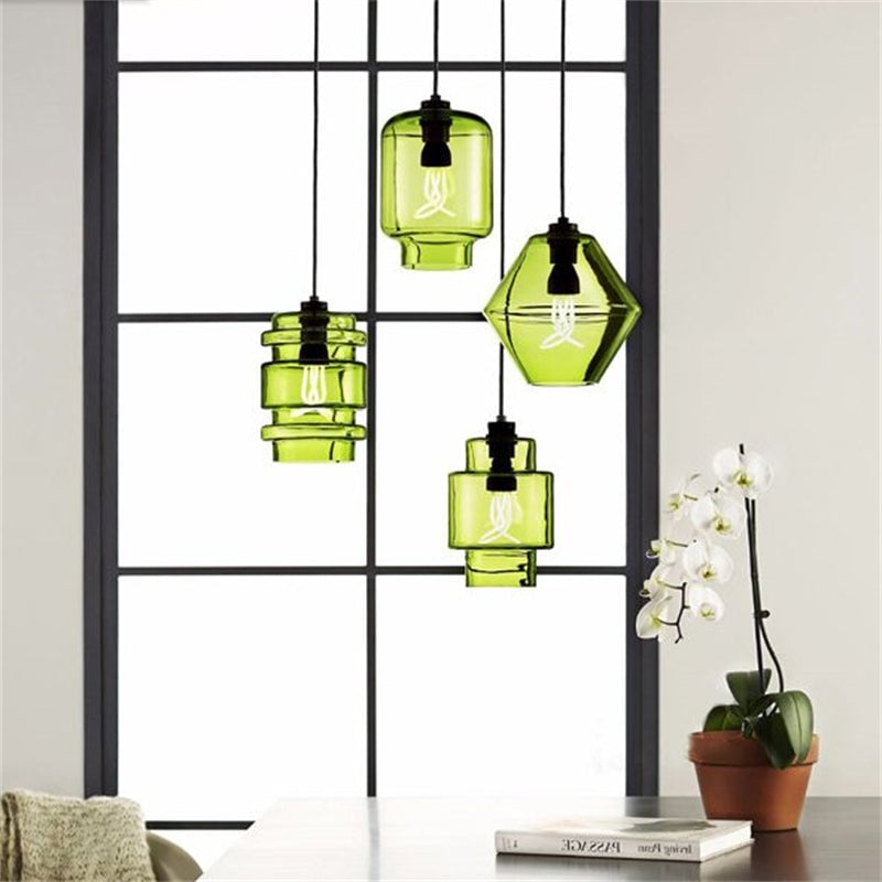 Four green glass pendants in different geometric shapes above a table beside a window