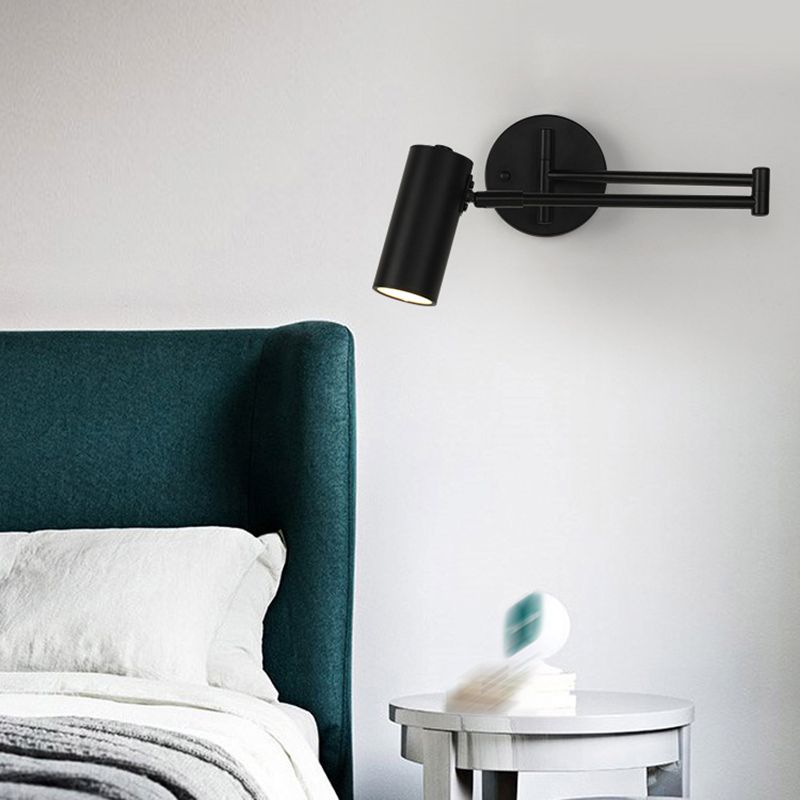 Brady Black cylindrical wall light with folded arms above a green upholstered bed and white bedside table