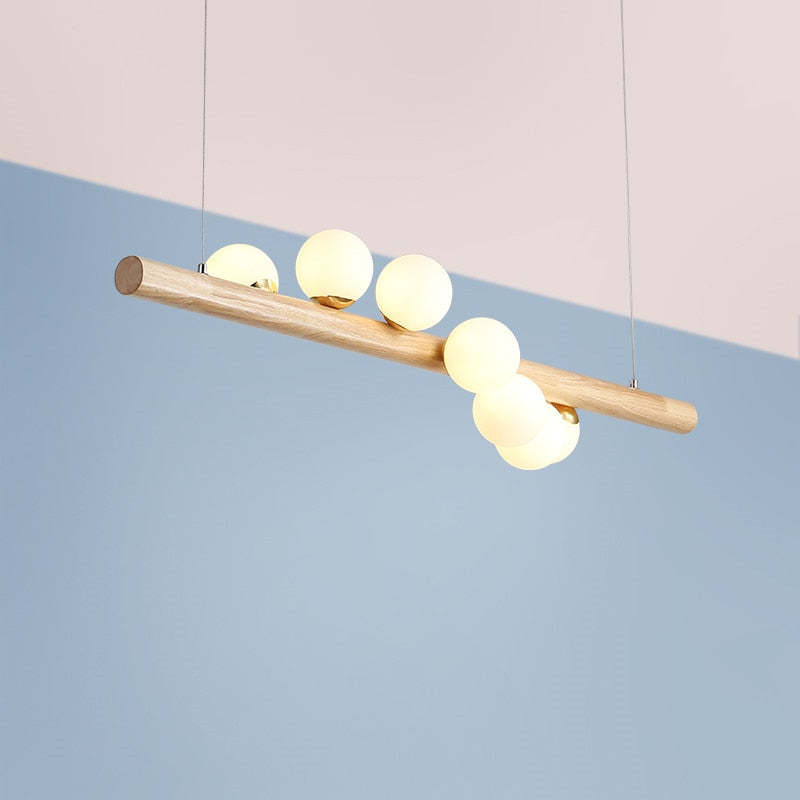 Light wooden bar pendant with five warm-looking globes and Gold-toned collars, shown at an angle against Pink and Blue