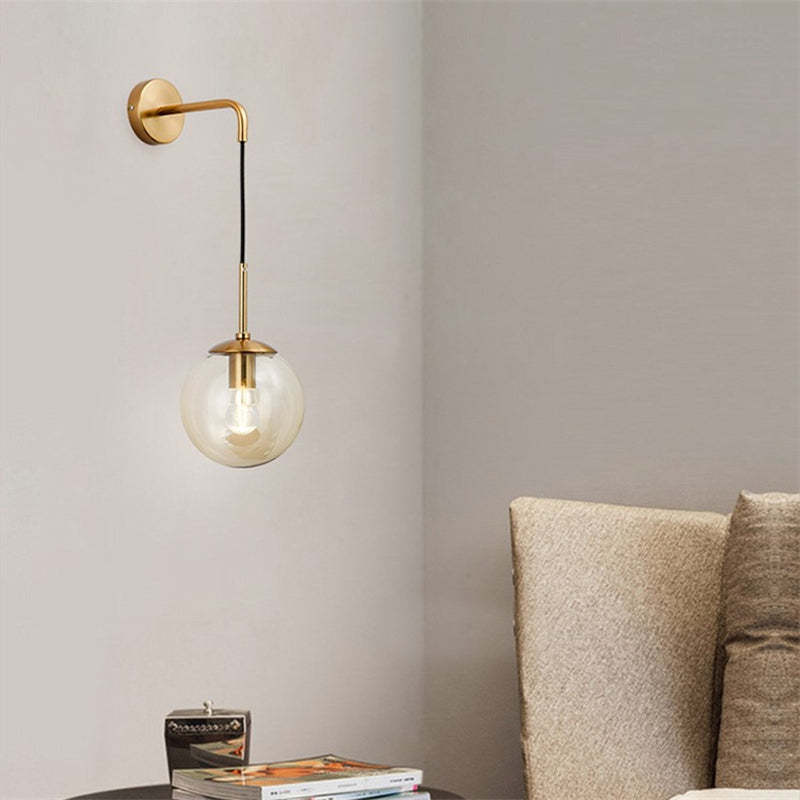 Gold-tone globe wall light beside a beige sofa and a side table topped with books