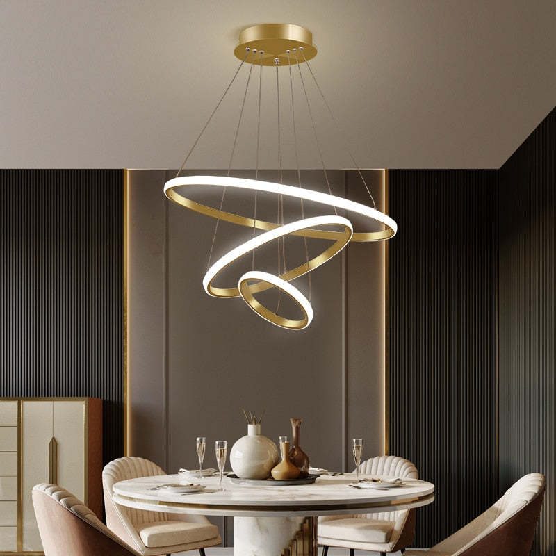 Golden three-ring pendant light above a round dining table with Cream chairs, vases and wine glasses beside a Dark slat wall