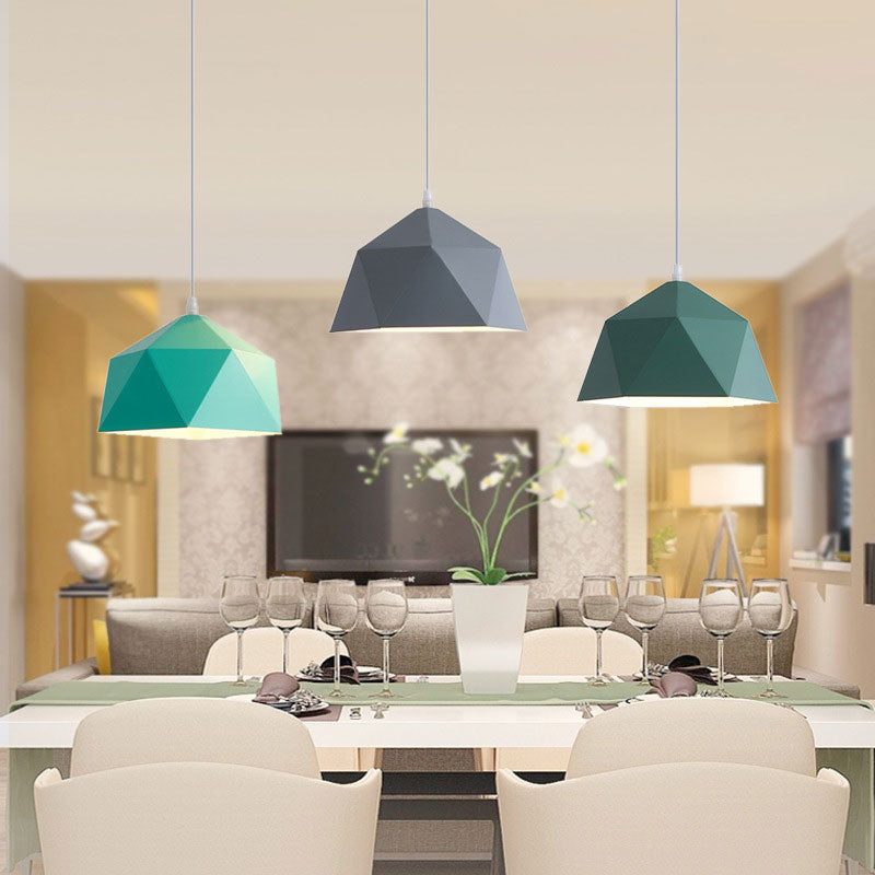 Three blue-and-green-toned geometric pendant shades above a dining table with pale chairs and wine glasses