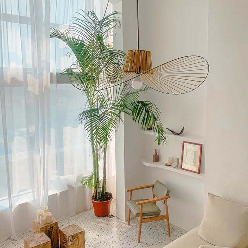 Golden-coloured wavy pendant with radiating lines near a potted palm, window and armchair