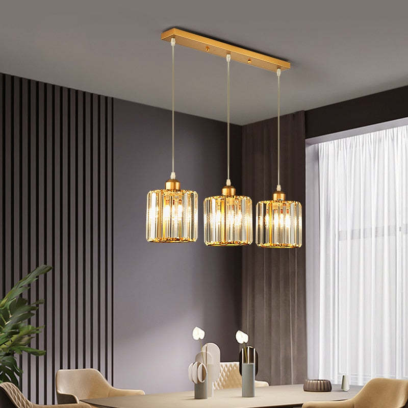 Gold three-cylinder glass row on rectangular canopy over dining table beside dark wall slats and sheer curtains