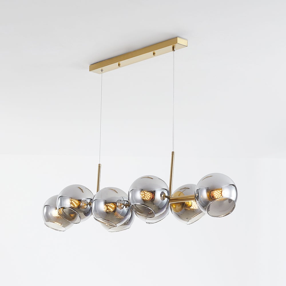 Gold rectangular canopy and two cables above gold linear pendant with darker reflective glass globes on pale background