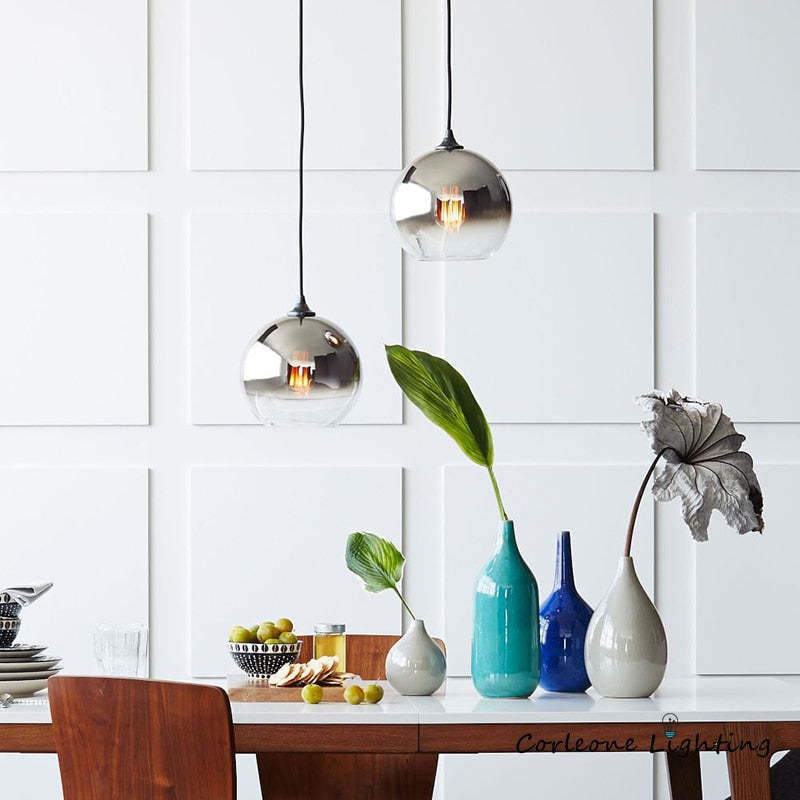 Two silver-gradient globe pendants above a dining table with colorful vases