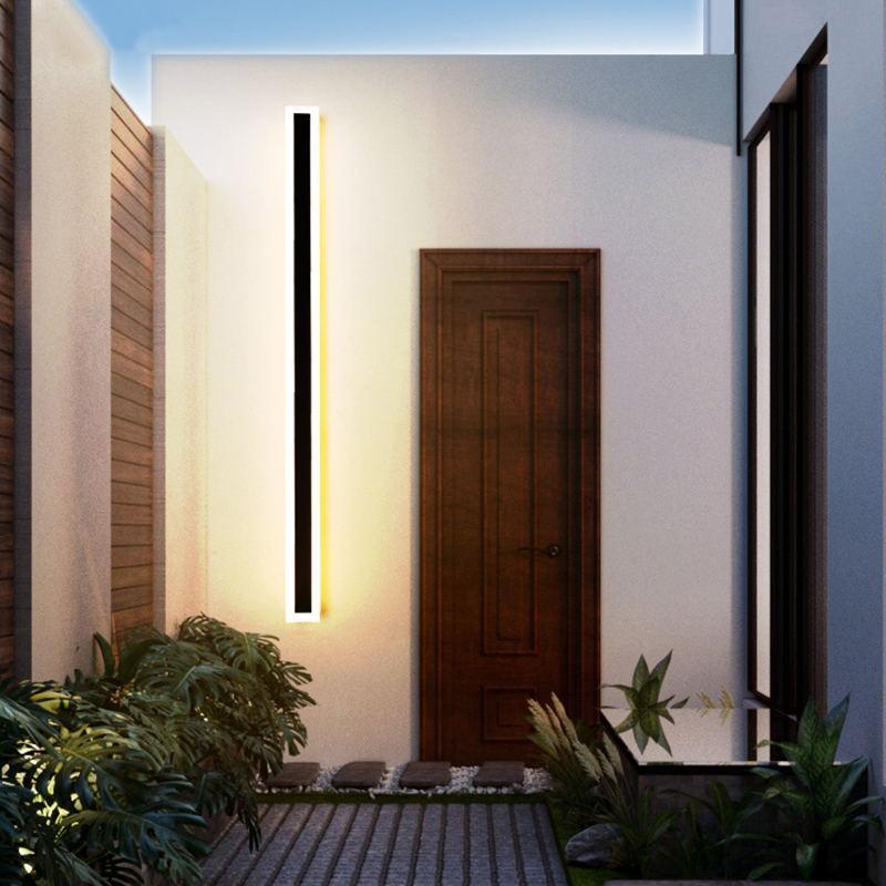 Long illuminated Edge wall light beside a wooden door in a planted courtyard