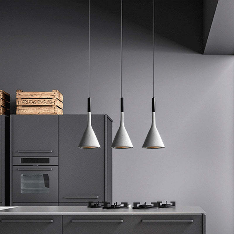 Three pale metal cone pendants in a row above a grey kitchen island with a gas hob and tall cabinetry