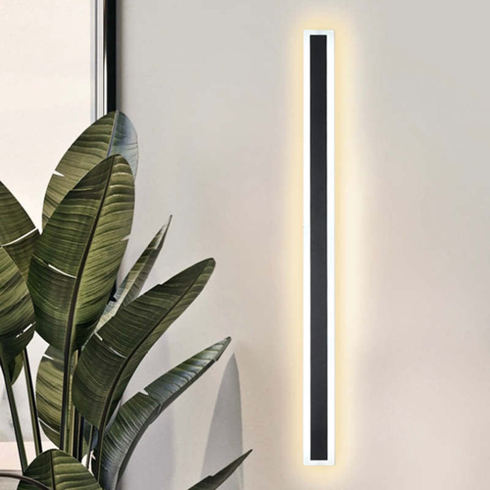 Edge wall light with a dark face and pale luminous border beside broad green leaves