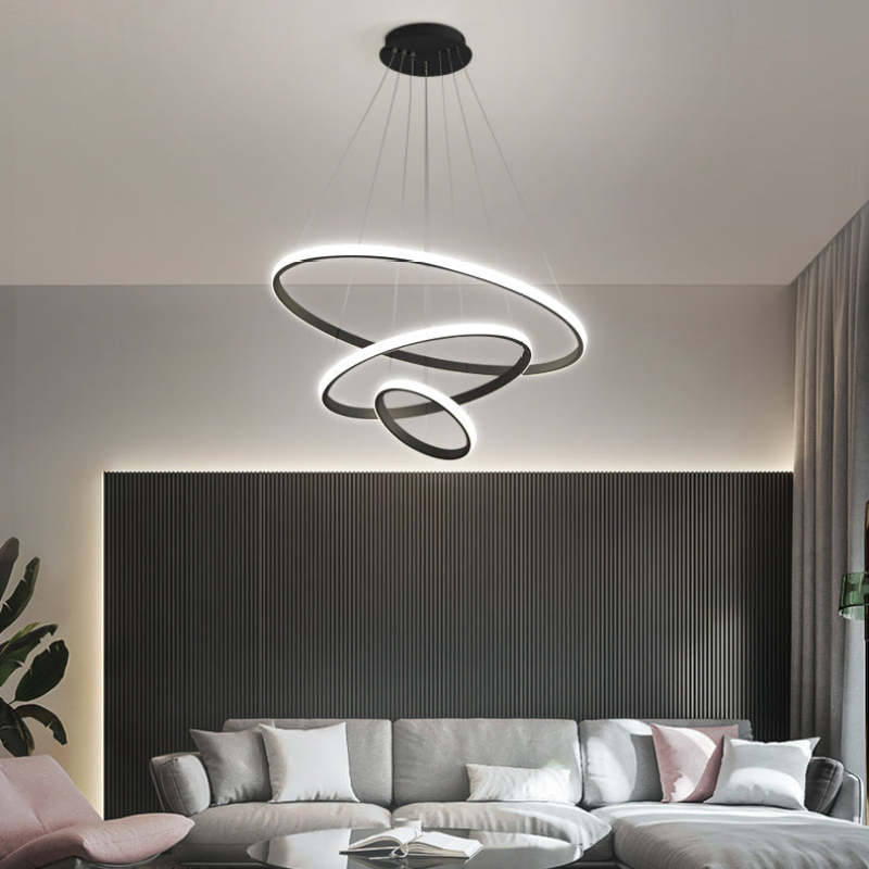 Black three-ring pendant light above a Gray sectional sofa, pillows and open book against a Dark slatted wall