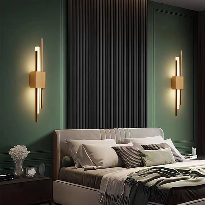 Two Gold Alana wall lights beside a bed on a dark green wall, with gold-tone centres and upper and lower light sections