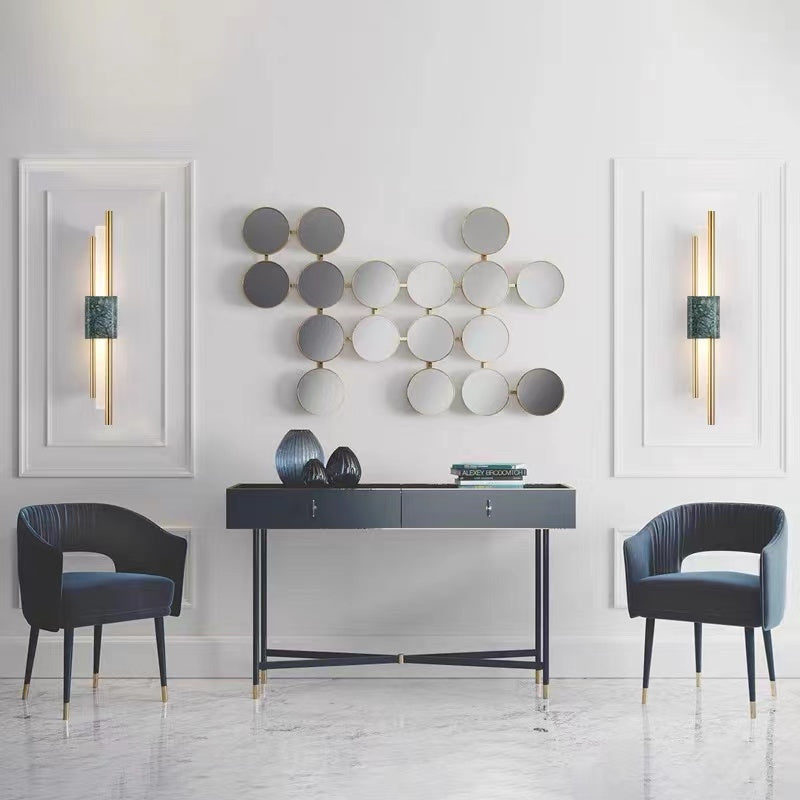 Two green-veined Alana wall lights beside circular wall art above a console between blue chairs