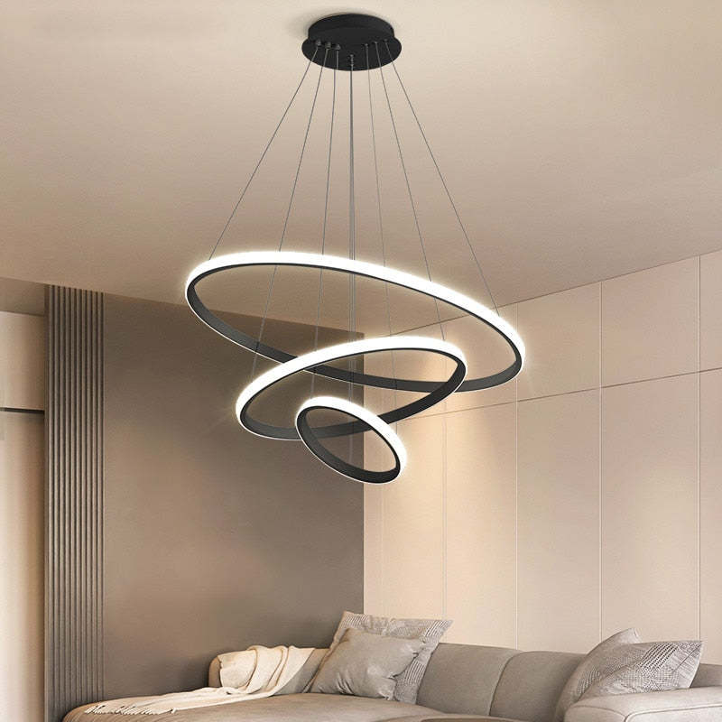 Black three-ring pendant light with illuminated outer bands above a Gray sofa and pale pillows beside curtains