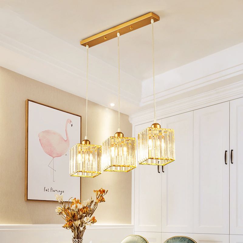 Gold three-square-shade row on rectangular canopy with flamingo artwork, flowers and white cupboard behind