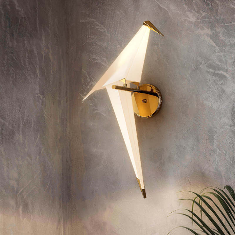 Single-bird Clifford wall light with round gold-tone plate on a grey wall above green foliage