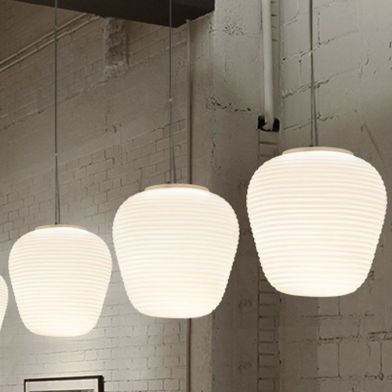 Three compact white ribbed pendants lit before a brick wall above artwork and a chair