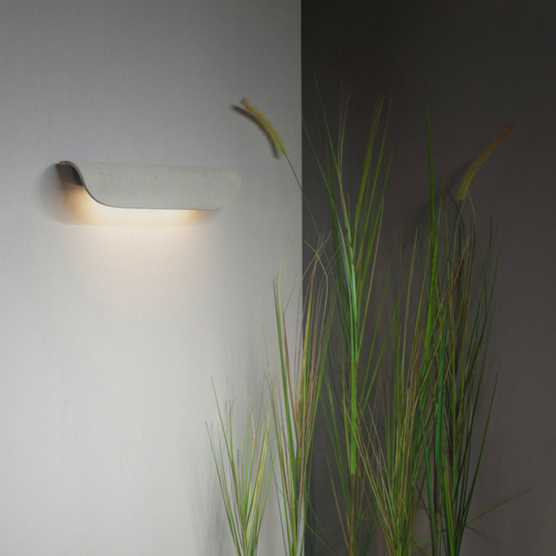 Pale textured curved wall light with a curled side profile beside ornamental grasses