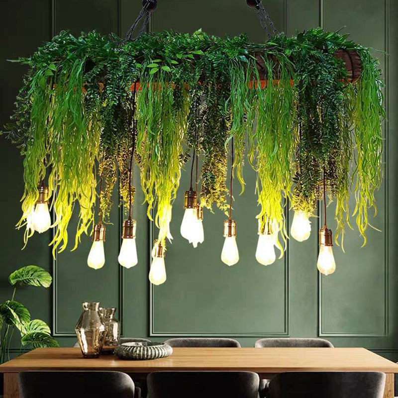 Lit foliage pendant above a wooden dining table beside a green wall.