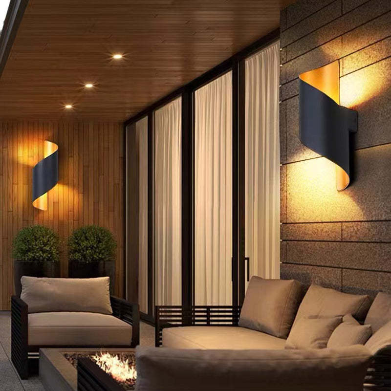Two black and gold wall lights casting upper and lower glow beside a furnished seating area and curtains