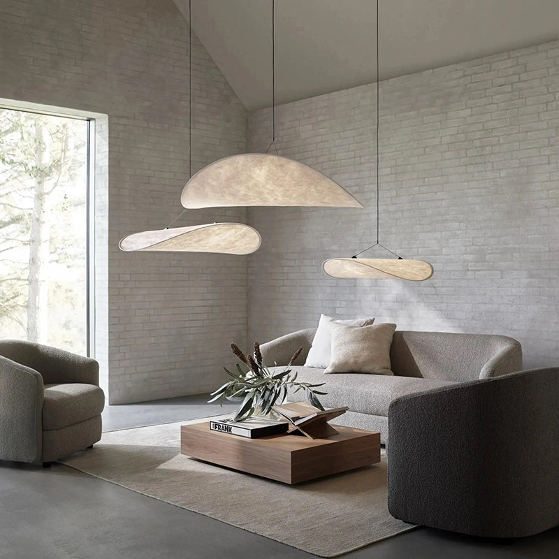 Three separate curved white pendants at different heights above gray seating and a low wood coffee table