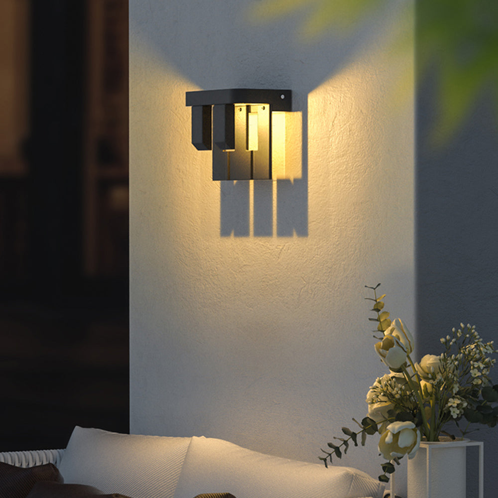 Orr 2-Light design on a grey wall above seating and a vase of flowers, with warm light through its staggered plates