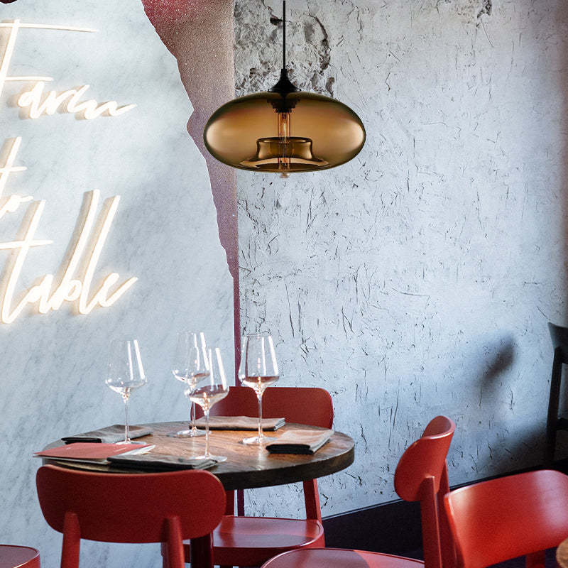 Brown-toned glass pendant light above a round table with Red chairs and wine glasses beside a textured wall