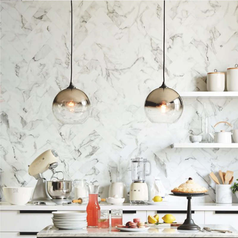 Two reflective globe pendants against a marbled kitchen wall