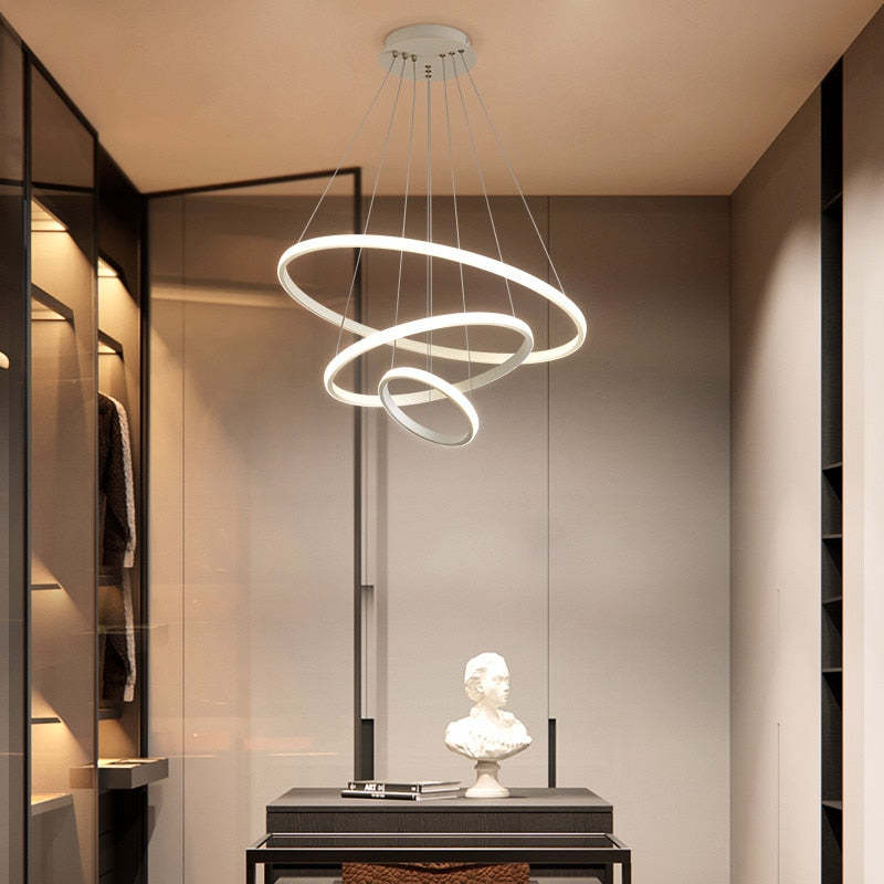 White three-ring pendant light above a Black console with books and a bust in a wardrobe room
