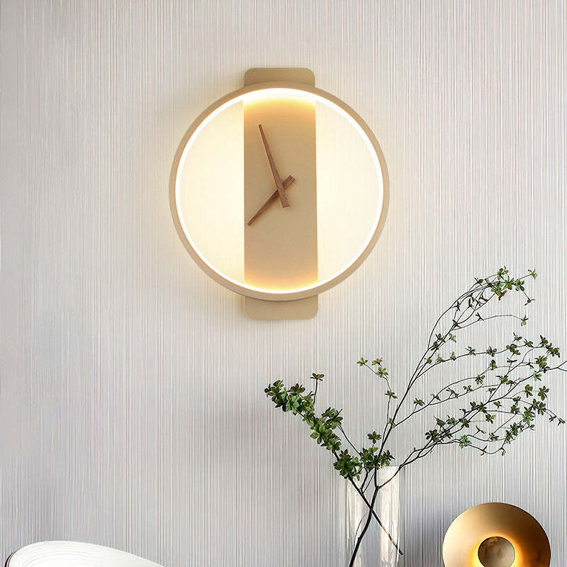 Lit round gold-tone Nielsen clock-face wall light on a textured wall beside branches and another lamp