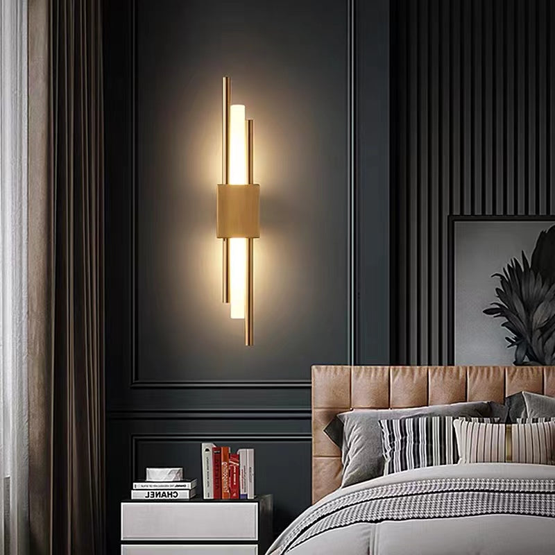 Gold-coloured Alana wall light on a dark panelled wall beside a bed and bedside books
