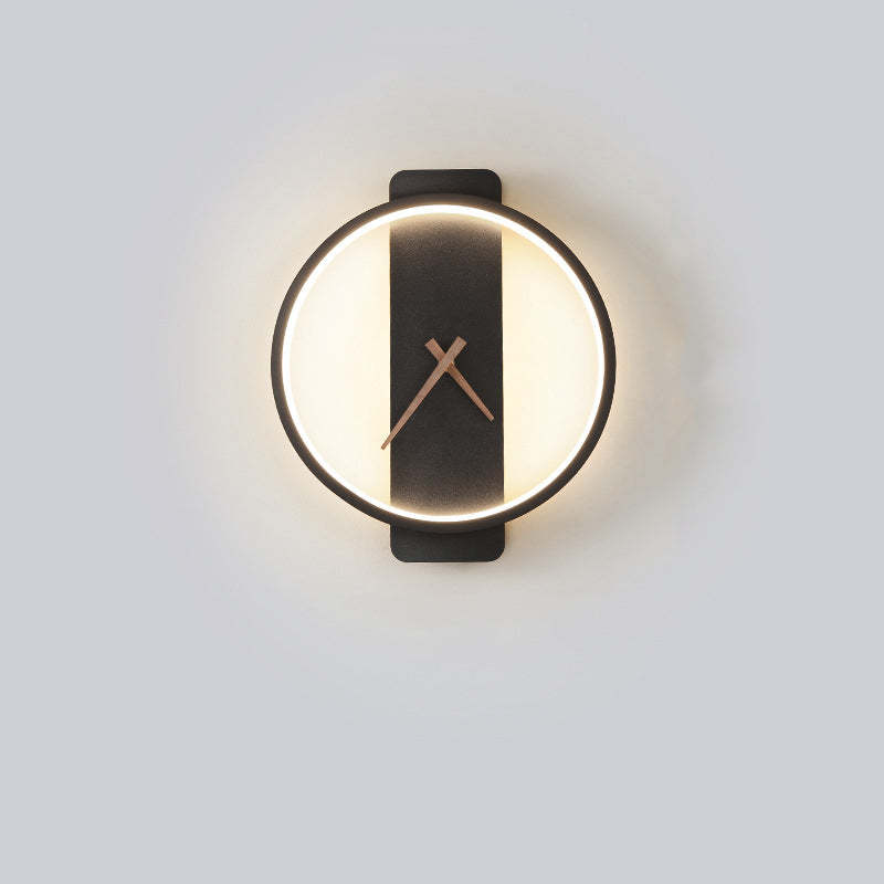 Black round clock-face wall light with a warm-looking halo and Brown hands against a Gray wall